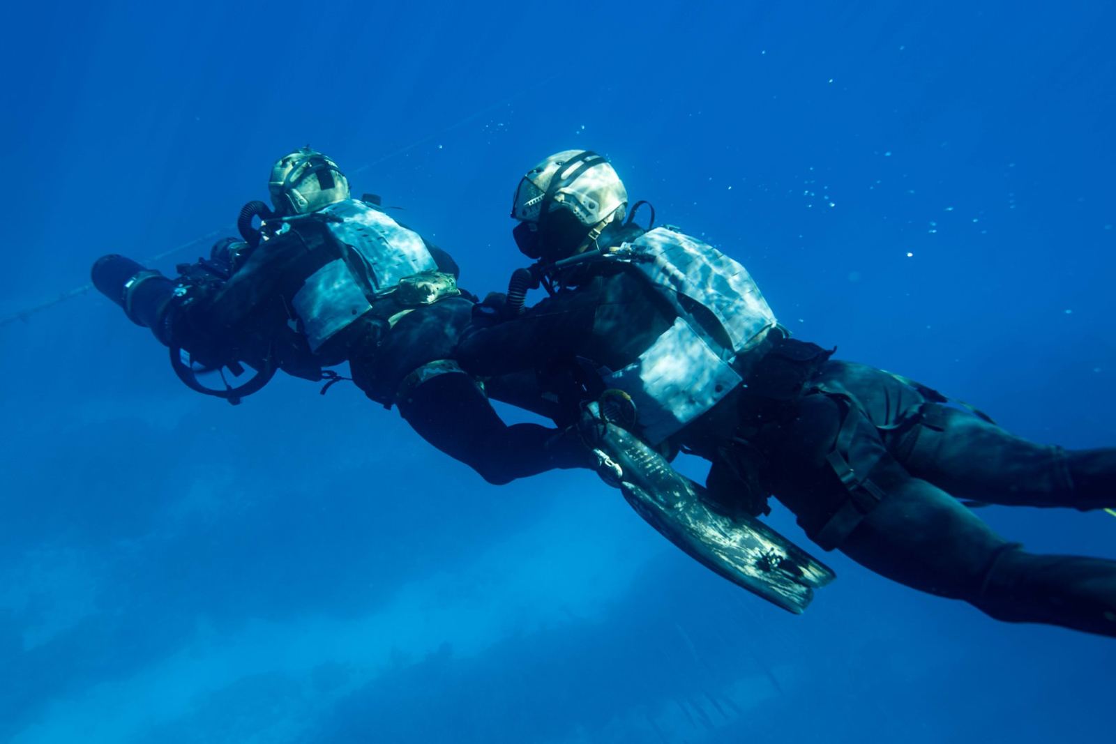 A pair of combat divers moving underwater with a diver propulsion vehicle