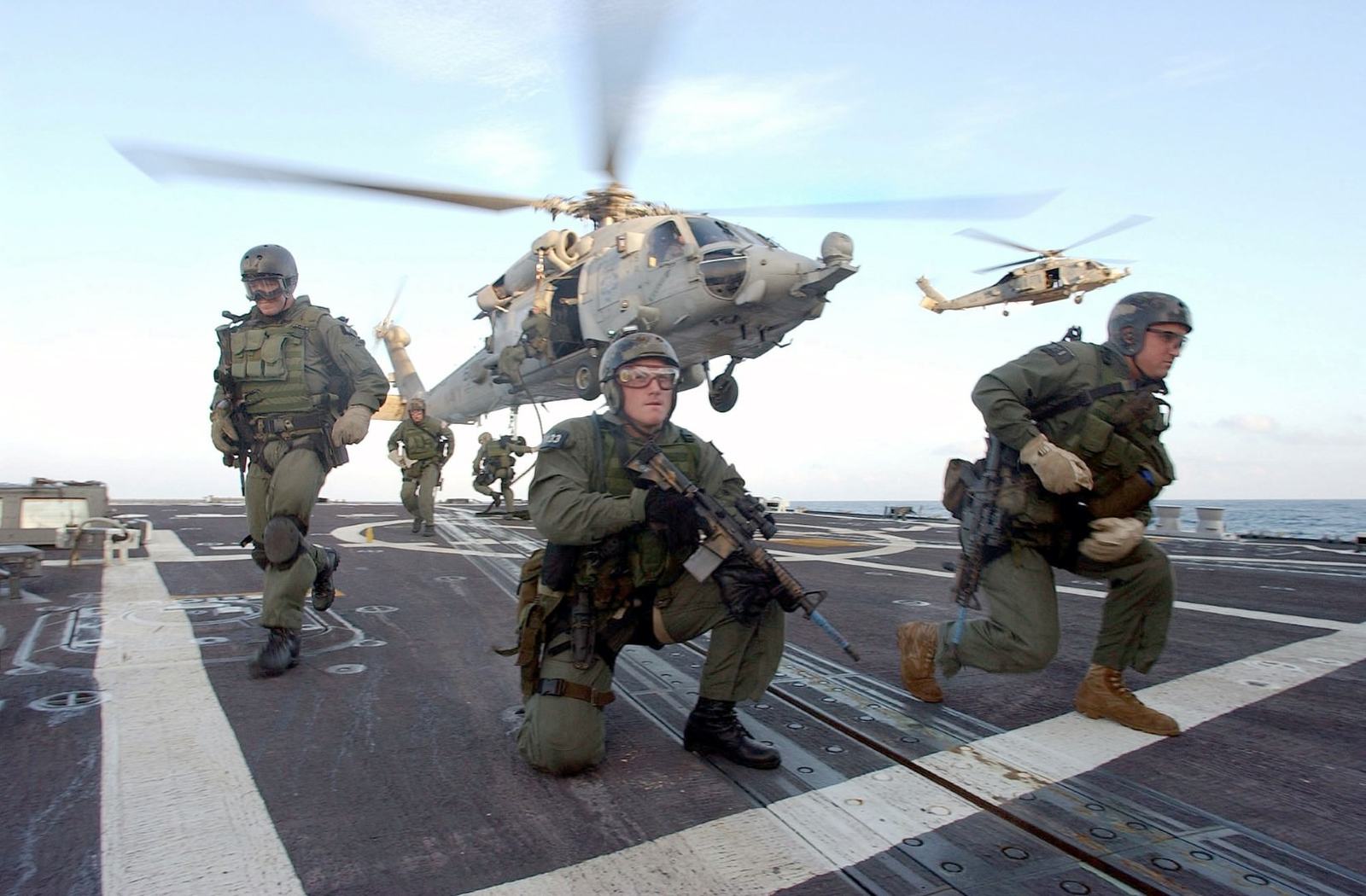 Naval Special Warfare operators moving across a flight deck toward waiting helicopters